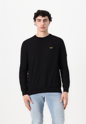 Zwarte gebreide trui met ronde hals en geribbelde manchetten. Bevat een klein gouden logo-opnaad op de linkerborst. Glad textuur.