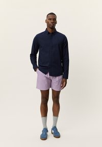 Μπλε ναυτικού χρώματος πουκάμισο με μακριά μανίκια, ροζ ριγέ σόρτς, μπλε αθλητικά παπούτσια και γκρι κάλτσες. Λείο ύφασμα, κλείσιμο με κουμπιά, άνετη γραμμή.