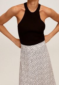 Sort ribbet halterneck-top parret med en hvid nederdel med et mønster af sorte prikker, der fremhæver en tætsiddende silhuet og tekstureret stof.