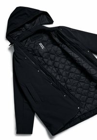 Parka nera con cappuccio, dotata di fodera interna trapuntata, chiusure a pulsante e tasche laterali. Materiale esterno liscio e design minimalista.