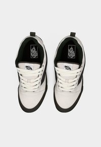 Λευκά και μαύρα αθλητικά παπούτσια με επάνω μέρος από σουέντ και καμβά, κλείσιμο με κορδόνια, λαστιχένια σόλα και επένδυση σε σκούρο πράσινο χρώμα. Το λογότυπο είναι ορατό στη γλώσσα.