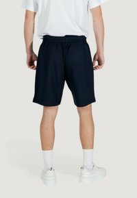 Pantaloni corti di tessuto blu navy con una cintura elastica, che arrivano sopra il ginocchio, abbinati a sneakers bianche e calze bianche di lunghezza media.
