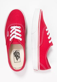 Røde kanvas kondiser med hvite snøringer, gummisåler og kontrasterende hvit søm. Vans-logo synlig på sålene. Klassisk låg-top design.