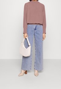 Top de manga larga color rosa con puños con volantes, combinado con jeans de pierna ancha de color azul claro. Sosteniendo un bolso color crema; usando zapatos de tacón beige.