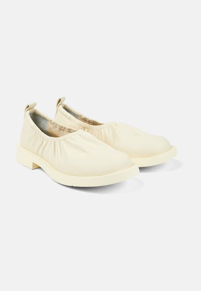 Light beige slip-on shoes with a gathered upper design, soft material, rounded toe, and a sturdy rubber sole.