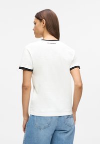T-shirt branco de manga curta com acabamento preto nas mangas e no decote, apresentando um discreto logótipo da marca cosido nas costas.