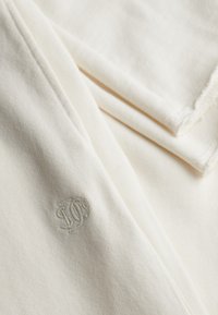 Lysegrønt bomuldsstof med foldede kanter. Har en lille, diskret broderet logo i en matchende lysegrøn farve. Blød tekstur.