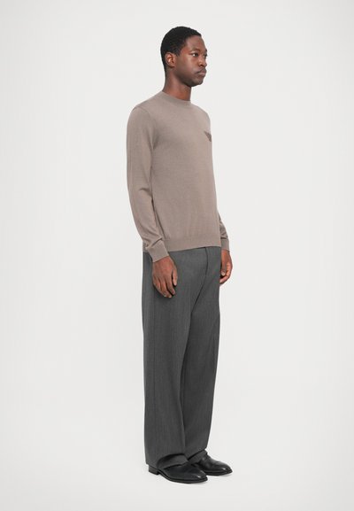 Brown knit sweater with long sleeves paired with gray wide-leg trousers. The outfit features a subtle logo detail on the chest. Black shoes complete the look.
