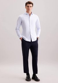 Camicia azzurro chiaro a maniche lunghe con colletto a punta, davanti con bottoni e vestibilità aderente. Abbinata a pantaloni blu scuro e scarpe nere.