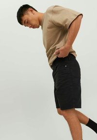 Pantaloni corti in denim nero con taglio dritto, abbinati a una camicia a maniche corte beige chiaro. L'outfit è completato da calze nere.