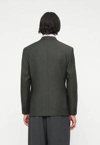 Dunkelgrüner Blazer mit strukturierter Form, Rückenschlitz und geknöpften Manschetten. Glatte Textur, von hinten betrachtet.