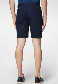 Granatowe szorty o gładkiej fakturze, z tylnymi kieszeniami, prostym kroju i pewnym pasie. Noszone z czarnymi butami.