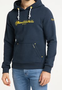 Mörkblå huvtröja i bomull med en framficka, med gula dragsnören och sömmar, samt logotypdetaljering på bröstet och ärmen.