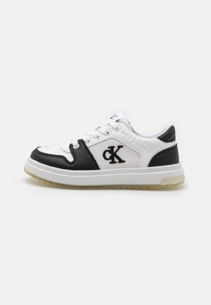 Flacher weißer und schwarzer Sneaker mit Schnürverschluss, Gummisohle und auffälligem schwarzen "cK"-Logo auf der Seitenfläche.