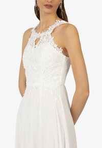 Mouwloze witte jurk met delicate bloemenkantdetails op het lijfje, een open sleutelgat en een soepel vallende rok.