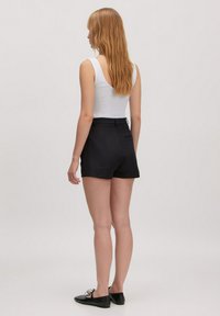 Zwarte op maat gemaakte shorts met een hoge taille, een gladde stof en een enkele achterzak. Gecombineerd met een witte tanktop en zwarte platte schoenen.