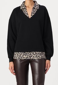 Felpa nera oversize con scollo a V profondo, caratterizzata da un collo e orlo con stampa leopardata. Abbinata a pantaloni lucidi in similpelle marrone.