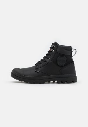 Schwarze Mid-Top-Stiefel mit Gummisohle, Schnürdesign und gepolsterter Knöchelunterstützung; mit einem Logopatch und strukturierten Stoffakzenten.