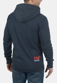 Sudadera con capucha en azul marino, fabricada en un tejido suave, con un logotipo en rojo y blanco en la parte inferior de la espalda y un corte relajado.