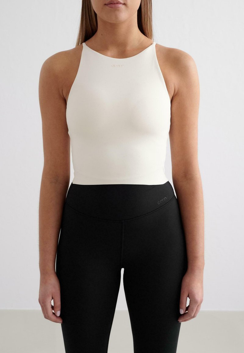Top sportivo bianco a collo alto in tessuto elasticizzato, con spalline sottili, abbinato a leggings neri a vita alta con un branding discreto.