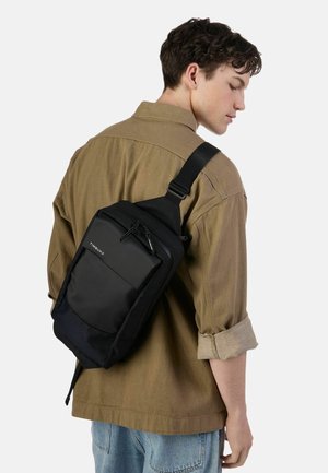 Zaino a tracolla nero realizzato con materiali resistenti, dotato di una tasca frontale con cerniera, tracolla regolabile e un design minimalista con marchio discreto.