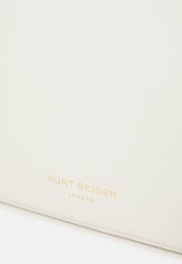 Vit läderväska med en slät yta och rektangulär form. Har den präglade texten "KURT GEIGER LONDON" i guld.