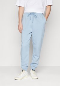 Světle modré tepláky vyrobené z měkké tkaniny, s elastickým pasem na šňůrky a malým logem na levém stehně.