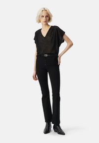 Blusa negra con encaje en la parte superior, escote en V y mangas cortas, combinada con unos jeans negros de campana con cierre de botones y un cinturón estrecho. Botines negros.