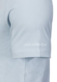 Chemise bleu clair à manches courtes avec le texte blanc "KARL LAGERFELD" brodé près de l'ourlet sur la manche.