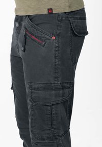 Zwarte cargobroek met meerdere zakken, rode ritssluiting als accent en een gestructureerde stof. Kenmerkt zichtbare stiksels en een logolabel op de tailleband.