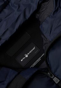 Marineblaue Segeljacke aus leichtem, ripstop Gewebe; verfügt über eine glänzende Oberfläche, ein Innenetikett und einen Reißverschluss.
