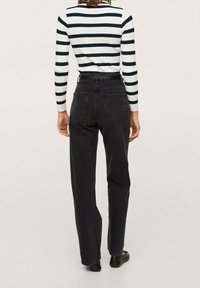 Schwarze High-Waist-Jeans mit geradem Bein, ausgestattet mit Gesäßtaschen und Gürtelschlaufen, kombiniert mit einem gestreiften Langarmshirt.