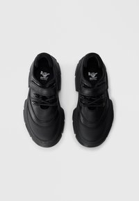 Chaussures en cuir noir avec une finition texturée, dotées de lacets et d'une bande Velcro, bout rond, et semelle en caoutchouc épaisse avec un léger profil.