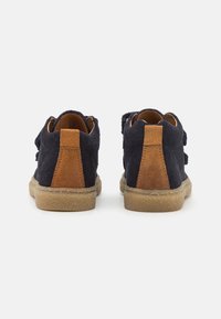 Zapatos de ante azul marino con acentos de ante marrón en el tacón y suela de goma texturizada; cuenta con dos correas de velcro ajustables para el cierre.