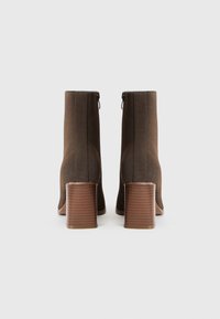 Bottines en suède marron avec talons carrés empilés et fermetures éclair à l'arrière, vues de dos sur un fond clair uni.