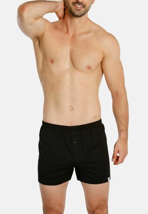Black cotton boxer shorts with elastic waistband, a front button closure, and a small logo tag on the lower left side.