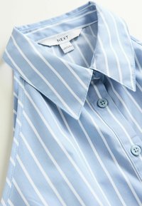 Blouse sans manches bleu clair avec des rayures verticales blanches, col classique et boutons bleus. Tissu doux avec une texture lisse. Étiquette de marque visible.