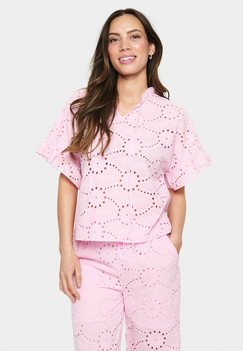 Top in tessuto eyelet rosa con cappuccio e maniche corte, caratterizzato da motivi floreali a intaglio. Pantaloni coordinate. Tessuto morbido.