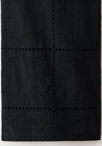 Tissu noir avec motifs floraux brodés et rangées horizontales et verticales de trous ronds découpés formant un motif en grille.