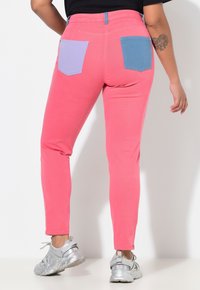 Dopasowane różowe dżinsy z kontrastowymi fioletowo-niebieskimi naszywkami na kieszeniach, z detalem zamka błyskawicznego na kieszeni, uzupełnione srebrnymi tenisówkami.