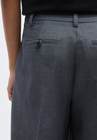 Γκρι παντελόνια σε ραμμένη εφαρμογή με λείο ύφασμα, πίσω τσέπη με κουμπί και δομημένη μέση. Απλός, καθαρός σχεδιασμός χωρίς διακοσμητικά στοιχεία.