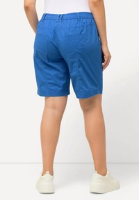 Blå shorts med elastisk midja och två bakfickor, med en mjuk yta och en avslappnad passform, tillsammans med vita sneakers.