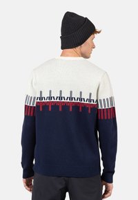 Dunkelblauer Strickpullover mit cremefarbenem oberen Abschnitt, der ein rot-blaues geometrisches Muster über der Brust aufweist. Rippbündchen und -saum.