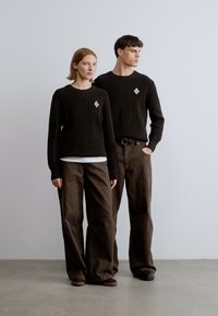 Pulls en tricot marron avec texture côtelée, manches longues et accents en forme de losange ; assortis à un pantalon marron large. Design simple et minimaliste.