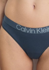 Nærbilde av mørkeblå Calvin Klein undertøy med en merkebånd, som viser stoffets tekstur mot en naturlig hudtone.