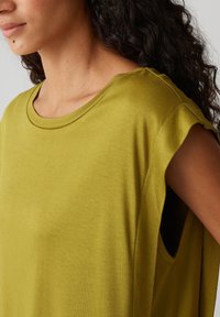 Top corto verde oliva a maniche corte con scollatura rotonda e tessuto morbido. Presenta ampie aperture per le braccia e un design rilassato.