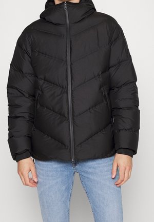 Svart pufferjacka med luva, med cheeron-sömmar, dragkedjefickor och elastiska ärmavslut. Slät struktur med en lätt design.