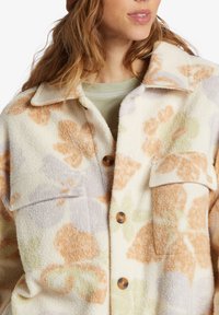 Flannel jacket with a soft, textured surface. Cream base with large floral patterns in orange, lavender, and green. Features chest pockets and buttons.