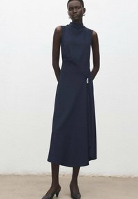 Granatowa, bezrękawnikowa sukienka midi z wysokim dekoltem, asymetrycznym krojem i bocznym detalem. Gładki materiał i luźny krój.