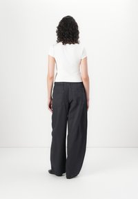 Black wide-leg pants with an elastic waistband and two back pockets, paired with a fitted white short-sleeve shirt.